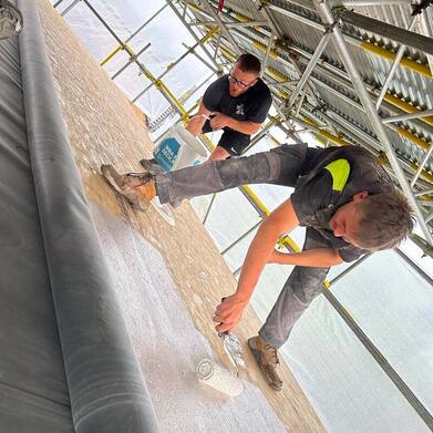 A picture of two roofers from the roofers sheffield team applying primer to a flat timber roof deck